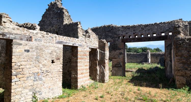 Stenen muren en bogen van een ingestort Romeins gebouw in Pompeii met Vesuvius in de verte.
