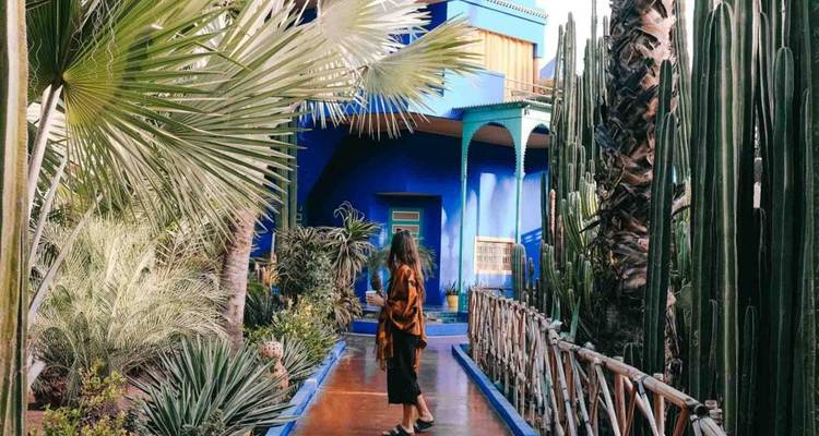 Una persona caminando en un jardín frondoso con un edificio azul al fondo.