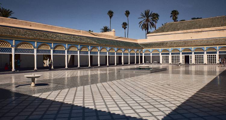An elegant courtyard with tiled floors and arches, surrounded by palm trees.