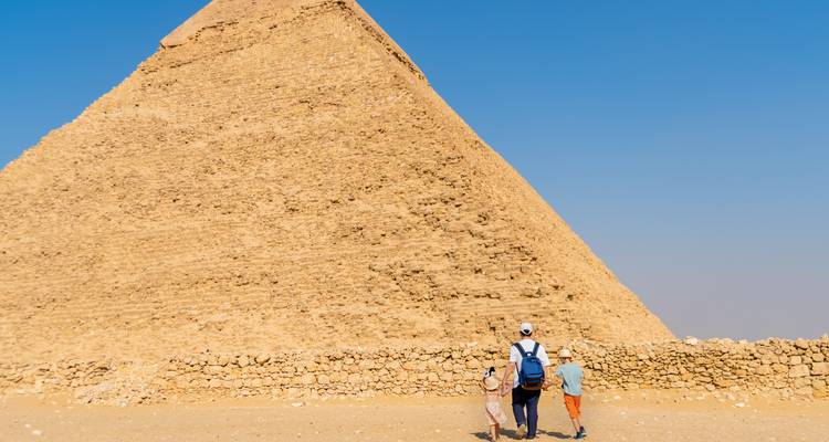 Un padre y dos niños caminando hacia la base de una pirámide gigante en el desierto