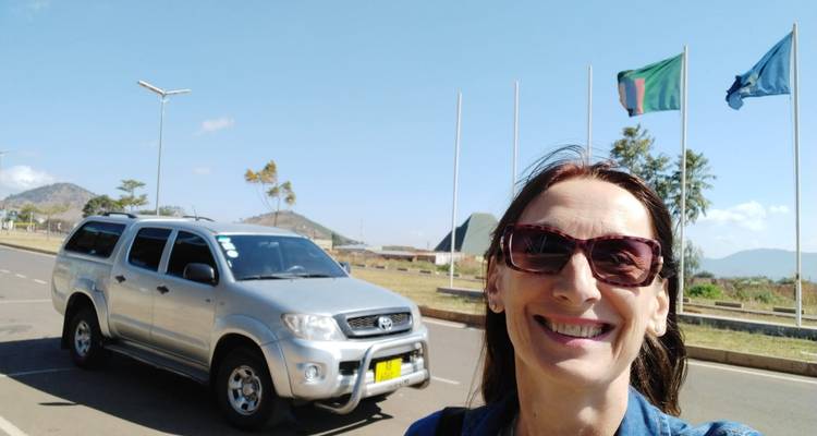 Smiling woman taking a selfie in front of a parked SUV.