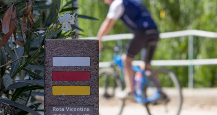 Ciclista junto a una señal de sendero con marcadores coloridos.