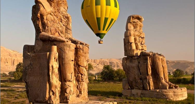 Un globo aerostático flotando sobre estatuas, con un fondo paisajístico.