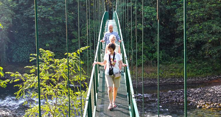 Reizigers steken een smalle hangbrug hoog boven een regenwoudrivier in Monteverde over.
