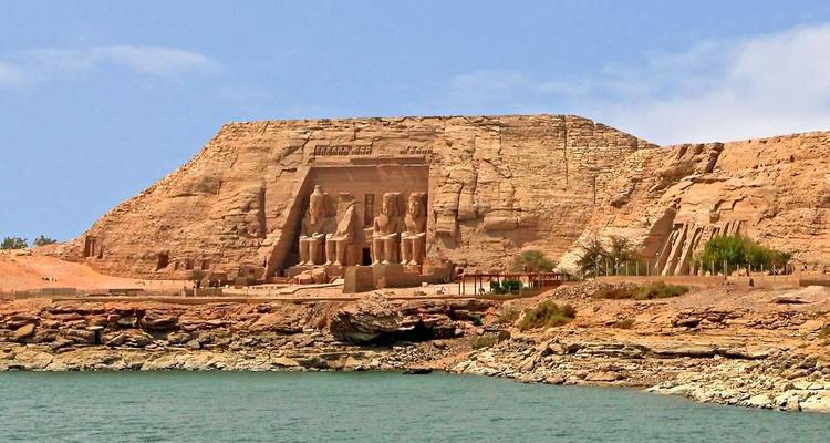 Temple d'Abu Simbel vu à travers une eau bleue calme sous un ciel lumineux.