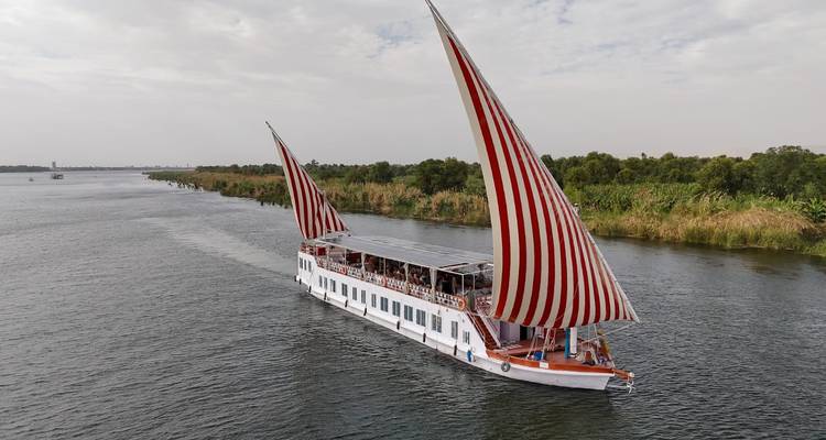 Un élégant voilier blanc aux voiles latines à rayures rouges frappantes navigue silencieusement sur le Nil.