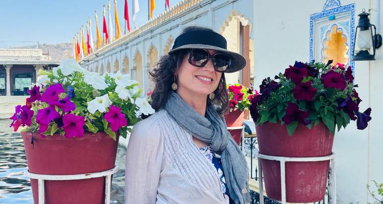 Woman smiling between two colorful flower stands beside a decorative palace pond.
