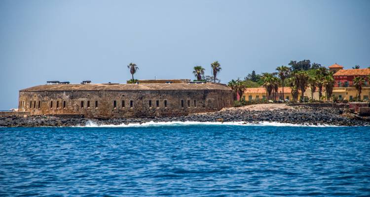 Stenen zeefort op Île de Gorée met palmbomen, uitzicht over het levendige blauwe Atlantische water.