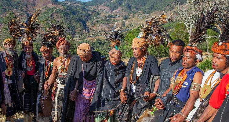 Line of Timorese villagers in colorful traditional dress holding hands during a ritual dance in the hills.