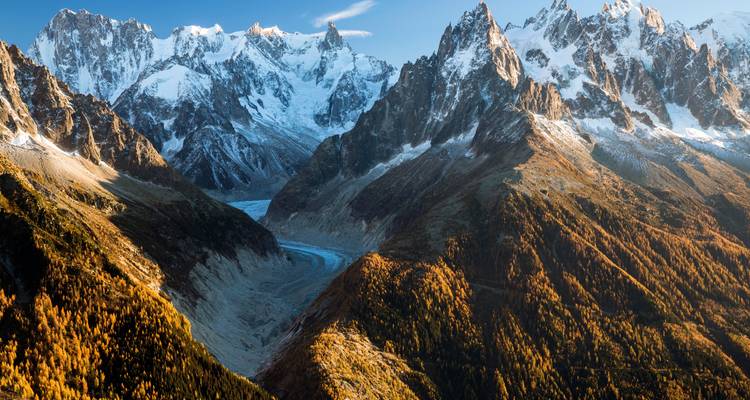 Vast mountainous terrain with a glacier and autumn-colored forests.