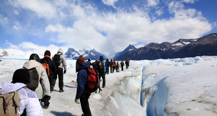 A group of people hiking across a glacier under a blue sky.