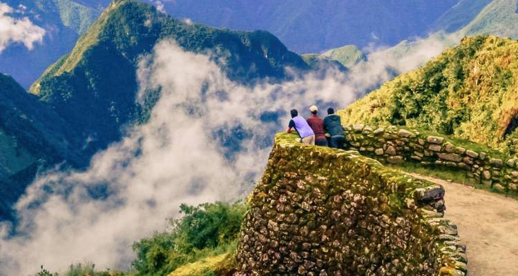 Hikers standing on ancient stone terraces overlooking misty green peaks of Machu Picchu region