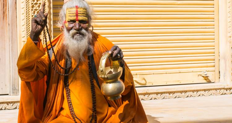 Man in traditional attire with painted face in front of a closed shutter.
