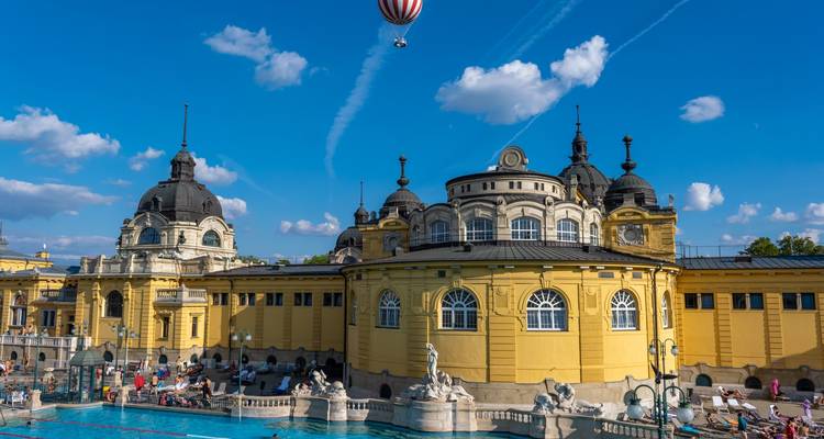 Piscine extérieure avec bâtiments historiques et personnes autour.