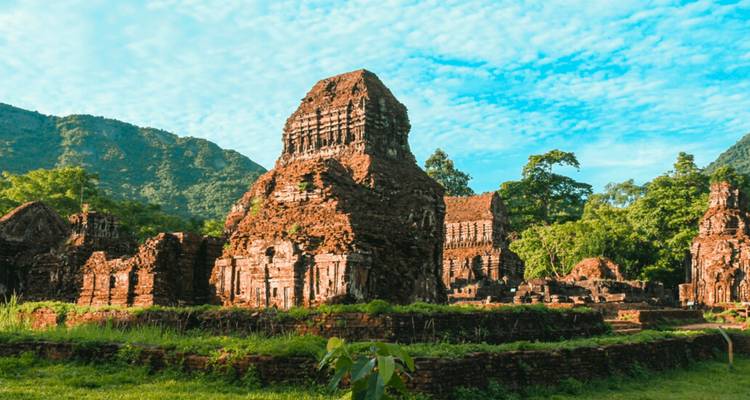 Ruïnes van een oude bakstenen tempel met bergen op de achtergrond.