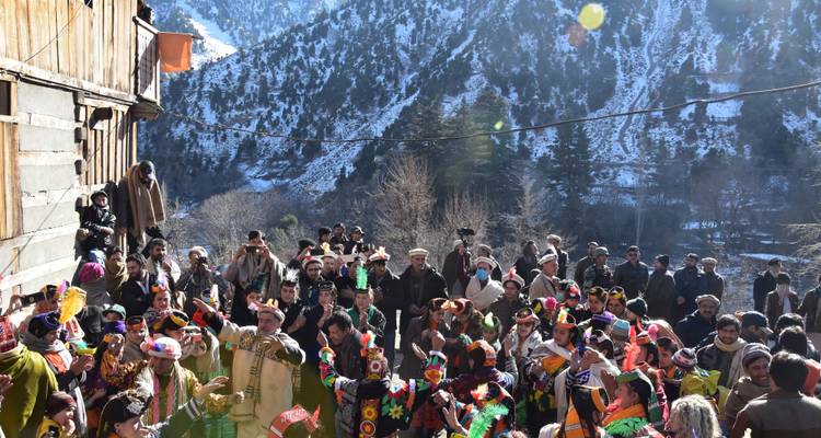 Versammlung von Menschen in traditioneller Kleidung inmitten schneebedeckter Berge.