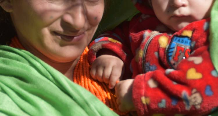 Nahaufnahme einer Frau, die ein Baby in heller Kleidung hält.