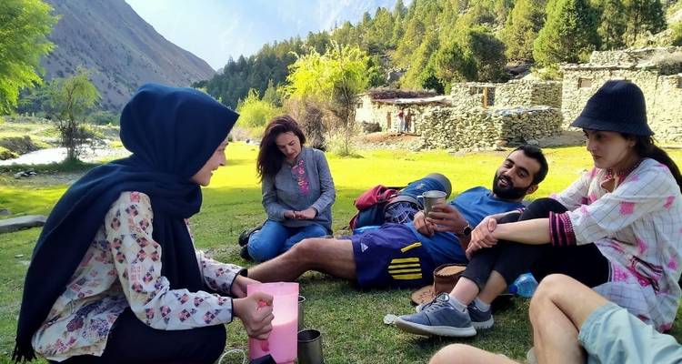 Menschen sitzen auf Gras in einer bergigen Dorfumgebung.