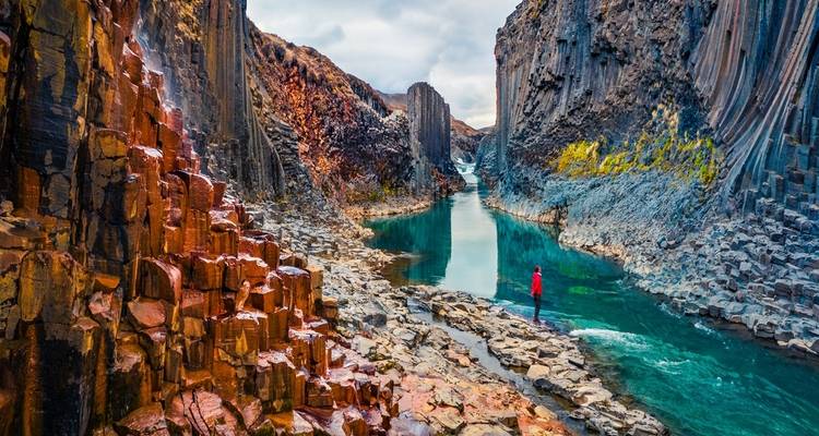 Kleurrijke kloof met basaltzuilen en een persoon die bij een rivier staat.