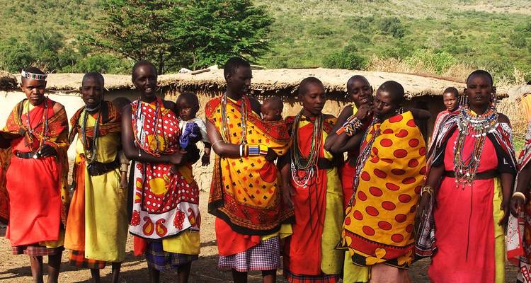 Group of Maasai women dressed in vibrant beadwork and patterned shukas stand in their village.