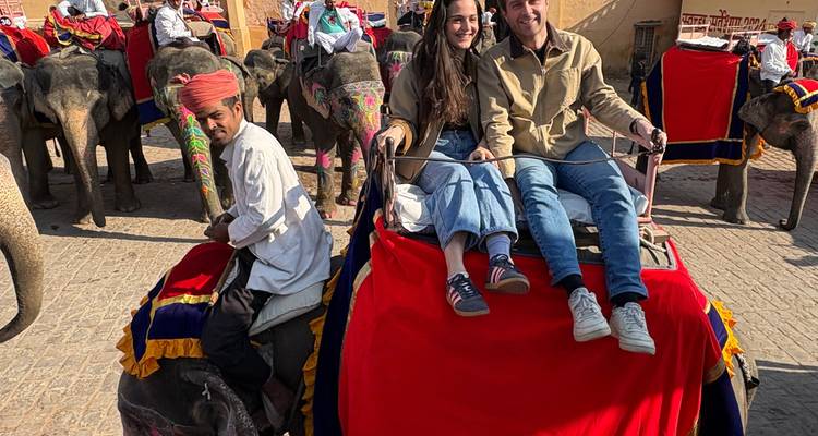 Toeristen rijden op een fel versierde olifant terwijl de mahout hen door een binnenplaats geleidt vol met andere olifanten.