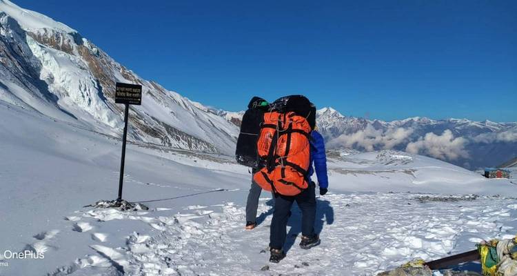 Persoon die loopt op een besneeuwde bergwandelroute met een grote rugzak.