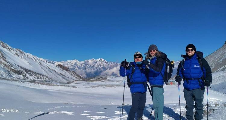 Drie mensen in blauwe jassen die op een besneeuwde bergwandelpad staan.