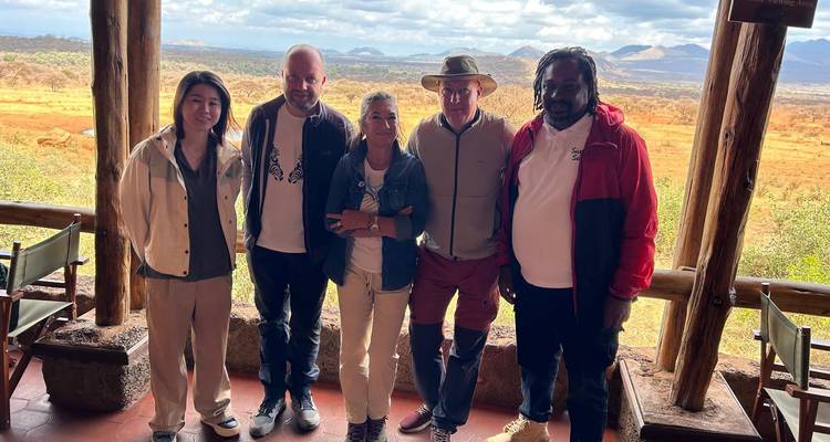 Group of travellers at a safari lodge balcony overlooking vast savanna and distant hills