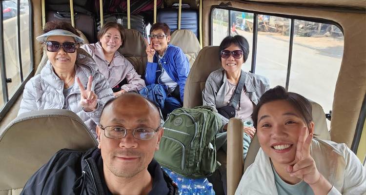 Six travellers smiling inside a safari minibus with luggage stacked overhead