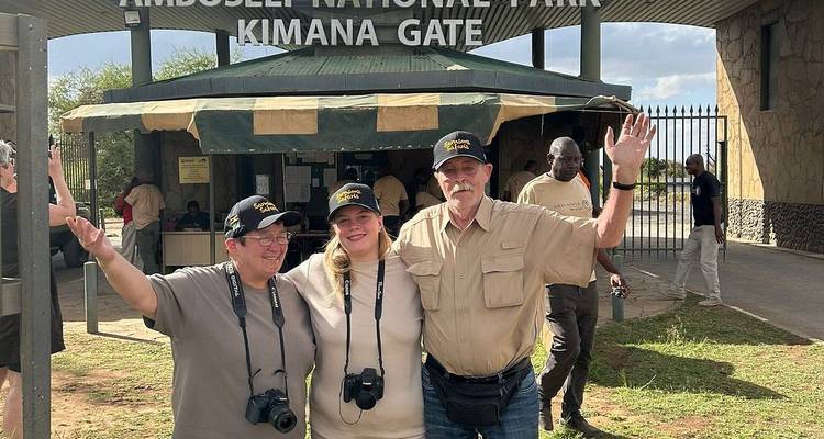 Three tourists celebrating beneath the Amboseli National Park Kimana Gate sign
