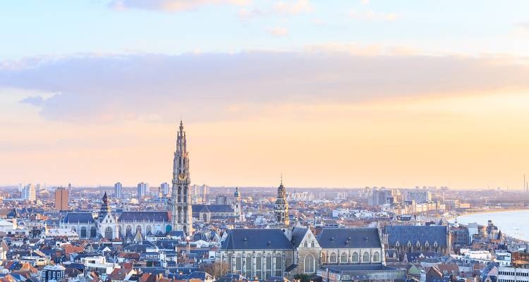 Panoramic sunset view over Antwerp with the Cathedral of Our Lady rising above the rooftops along the Scheldt River.