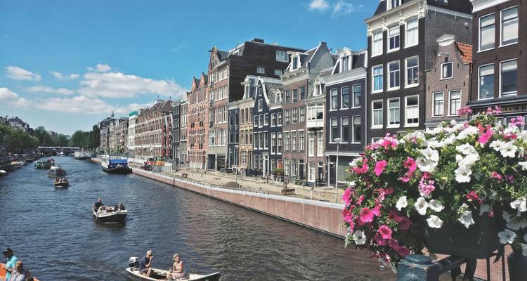 Sunny canal scene with classic gabled houses, small boats and flowers in a Dutch city.