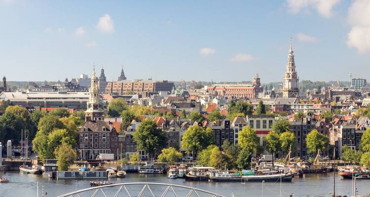 Elevated panoramic view of Amsterdam’s historic skyline with church towers and canals on a clear day.
