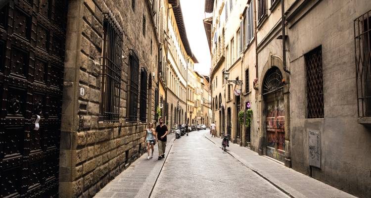 Rue médiévale étroite à Florence avec des piétons et des vélos garés.