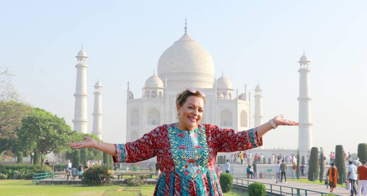 Person posing joyfully in front of the Taj Mahal on a clear day.