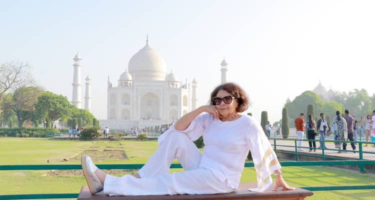 Woman in white outfit sitting with the Taj Mahal in the background.