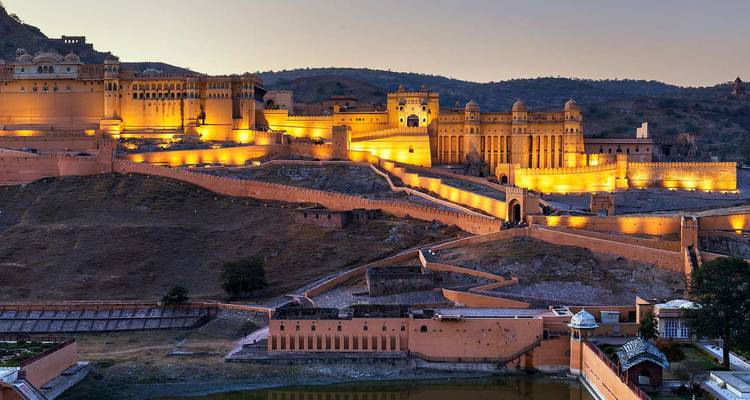 Amber Fort dramatically illuminated in golden lights at dusk, sprawling over a rugged hillside.