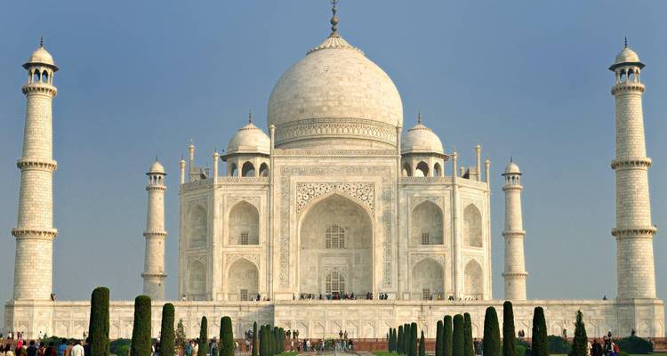 Iconic white marble Taj Mahal with its four minarets rising against a pale blue sky.