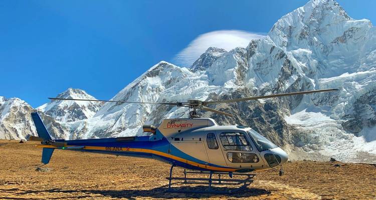 Helikopter op rotsachtig terrein met besneeuwde toppen op de achtergrond.
