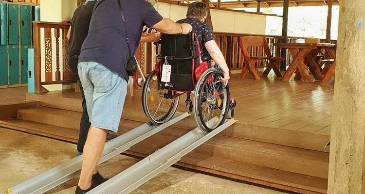 Person in wheelchair being assisted up a ramp.