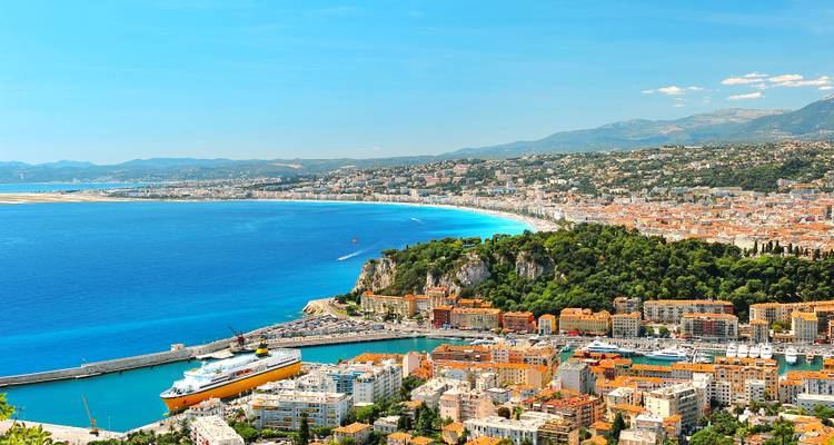 Coastal cityscape with blue waters and mountains in the distance.