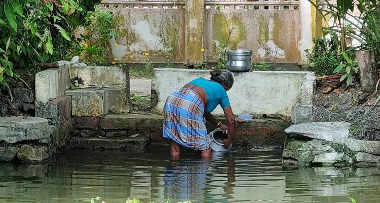 Eine Person, die Geschirr in einem kleinen Gewässer spült.