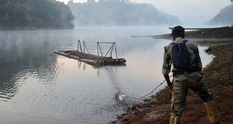 Person in einer Uniform nahe einem Fluss, mit Nebel und einem Floß.
