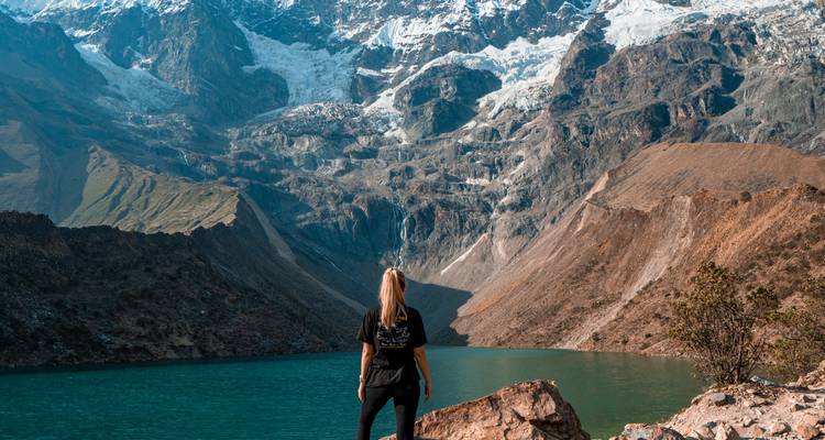 Personne debout près d'un lac bleu entouré de montagnes aux sommets enneigés.