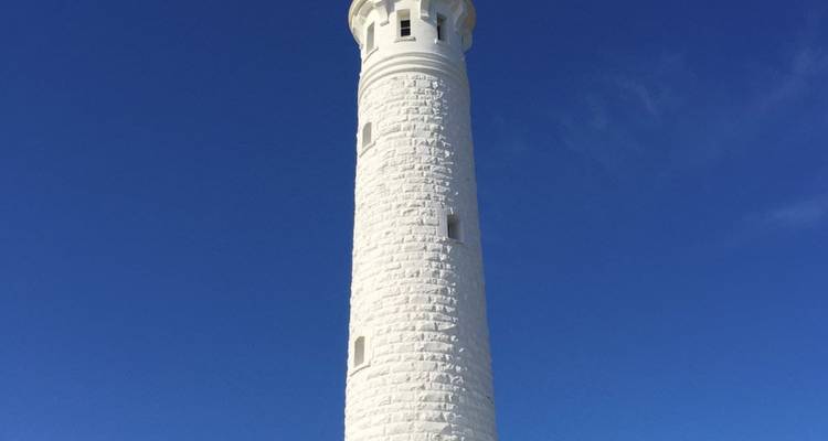 Een hoge witte vuurtoren staat tegen een levendige blauwe lucht in West-Australië.