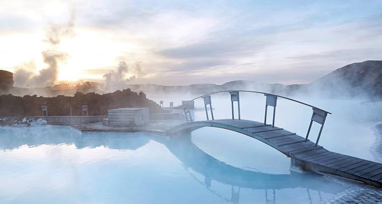Geothermal pool with steam and a bridge at sunrise.