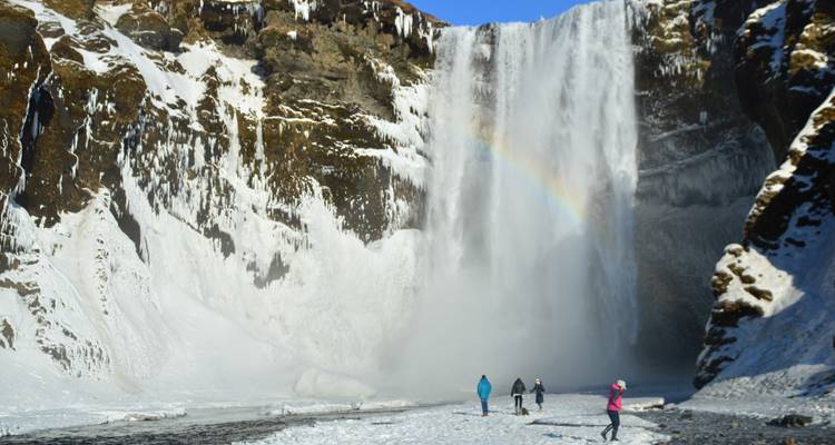 People standing by a large waterfall with a rainbow.