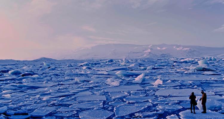 People walking among large ice sheets in a vast icy landscape.