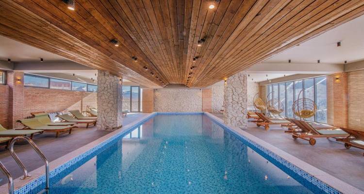 Binnenzwembad met houten plafond en ligstoelen.