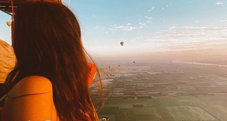 Frau in einem Heißluftballon mit Blick auf Felder und Fluss.
